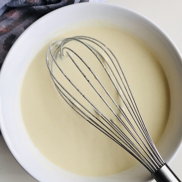 White round bowl containing pancake batter and whisk