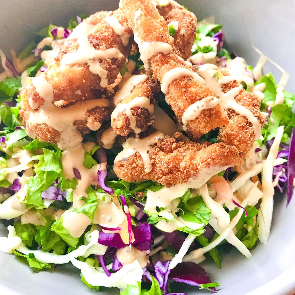 Chopped salad with chicken tenders on top and a salad dressing.