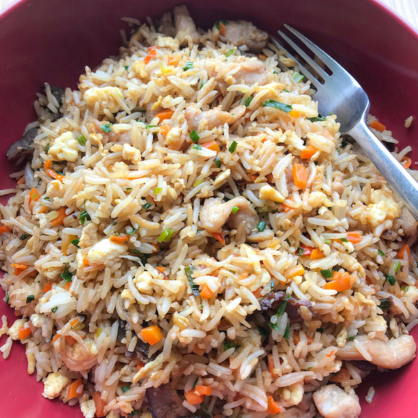 A round red bowl of fried rice with pork and biltong and a silver fork