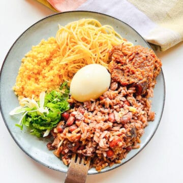 A plate of waakye with waakye stew, a boiled egg, gari, spaghetti and lettuce