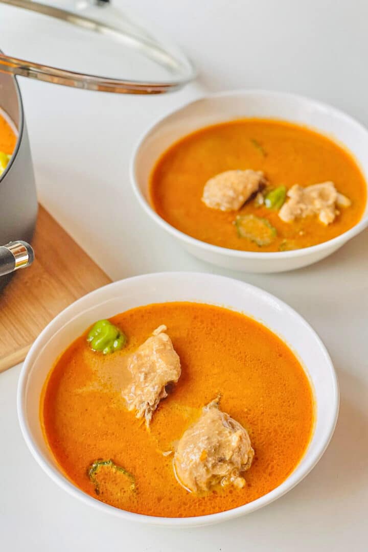Two white bowls of groundnut soup with chicken