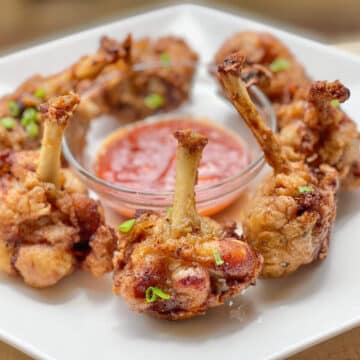 6 Chicken lollipops on a white hexagonal plate and a red dip in the middle.
