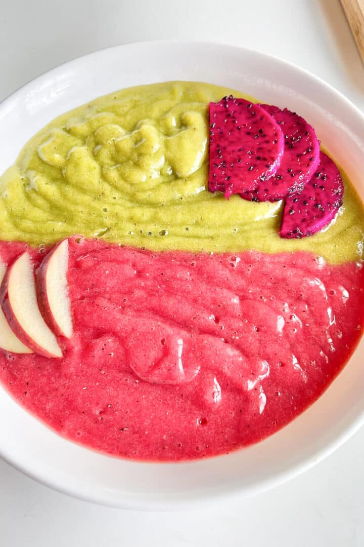 Green and red smoothie bowl with sliced apples and dragonfruit on top.