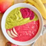 Green and red smoothie bowl with sliced apples and dragonfruit on top.