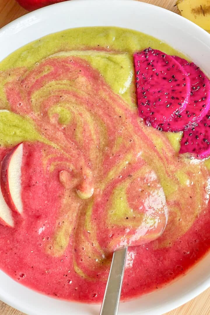 Green and red smoothie bowl with dragon fruit slices on top.