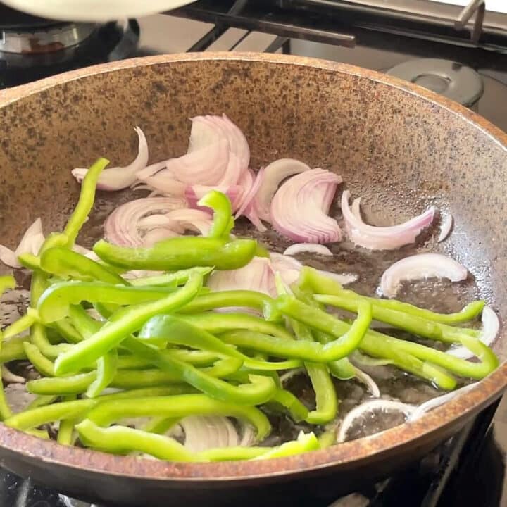 Pan with sliced green bell peppers and sliced onions.