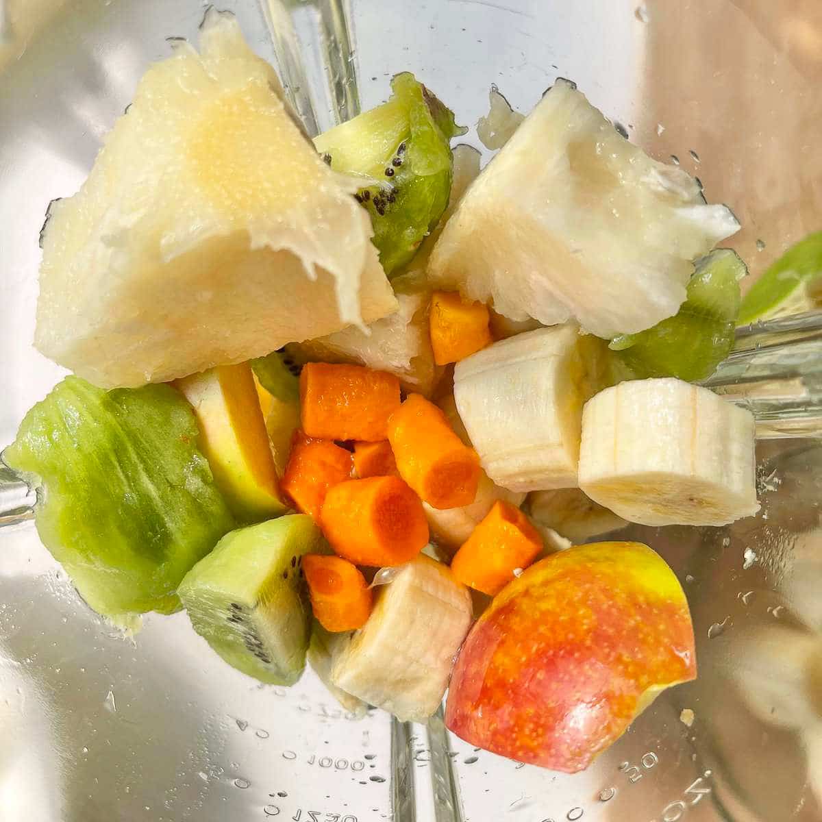 Chopped pineapple, bananas, apples, kiwi and turmeric in a blender