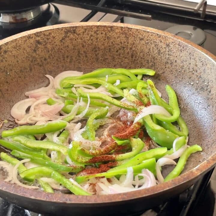 Pan with sliced green bell peppers and sliced onions with paprika powder sprinkled on top.
