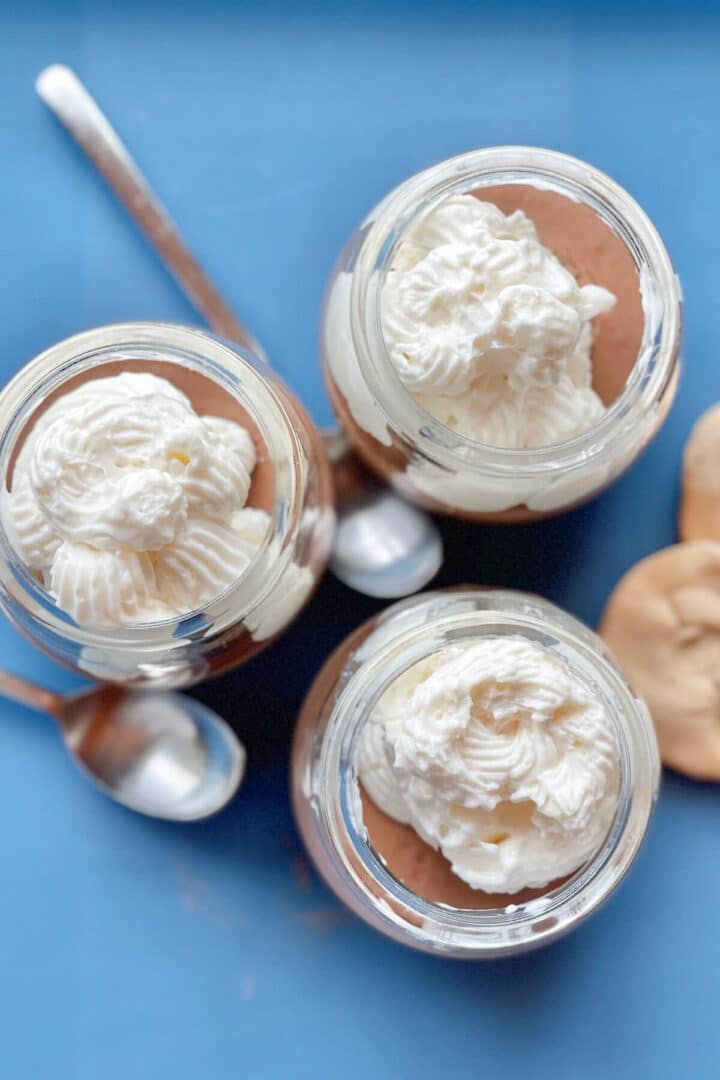 Three glass jars of chocolate pudding on a blue surface