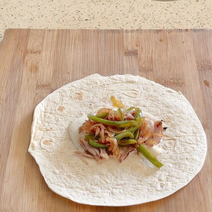 A small tortilla with onions and bell peppers on a wooden board.