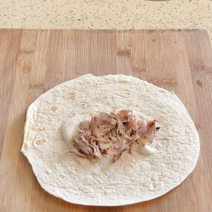 A small tortilla with chicken on top on a wooden board.