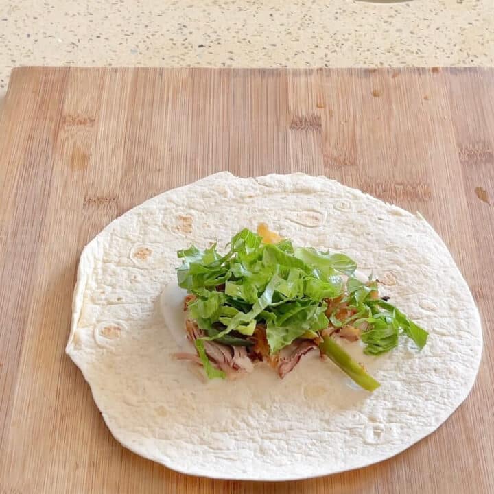 A small tortilla with lettuce on top on a wooden board.