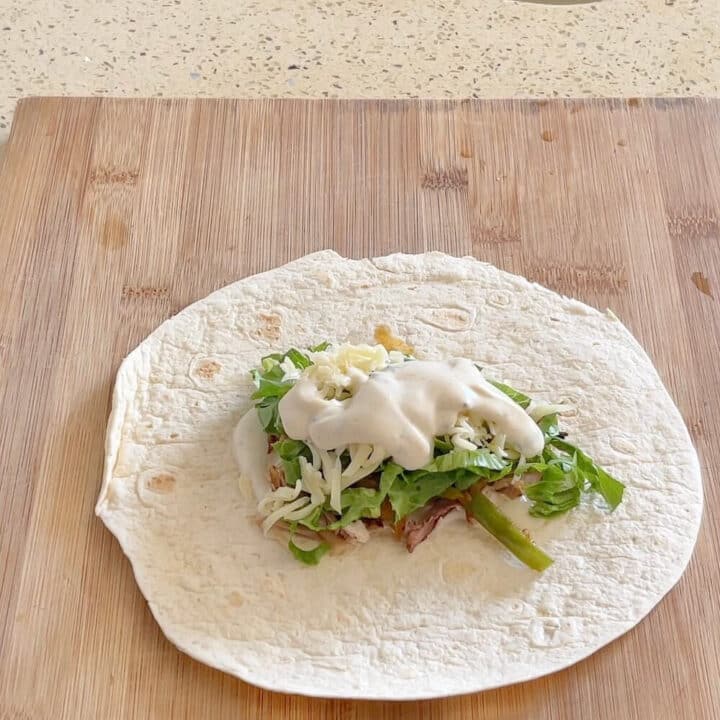 A small tortilla with mayo on top on a wooden board.