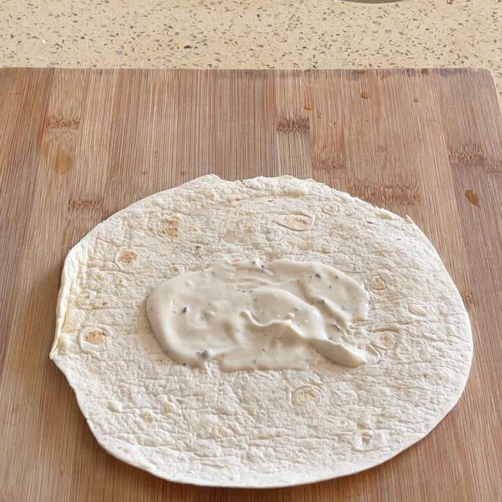 A small tortilla with mayonnaise smeared on a wooden board.