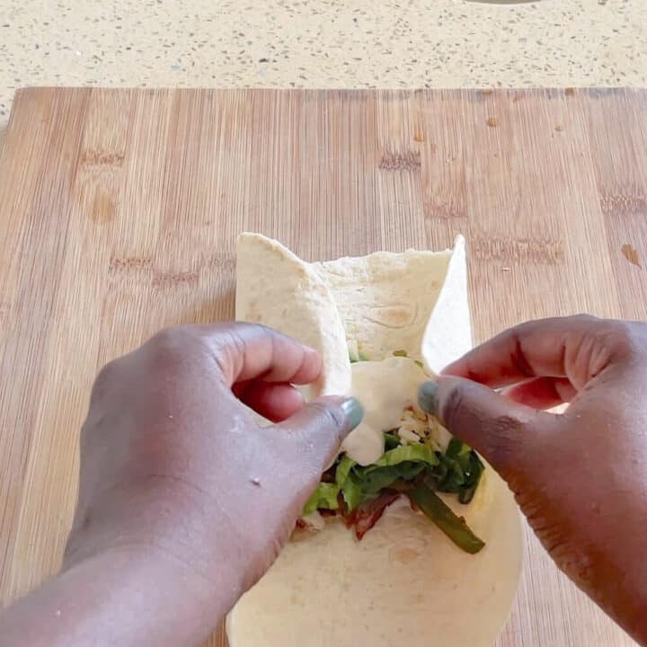 Tortilla being wrapped on a wooden board.