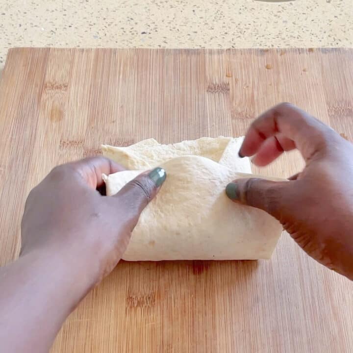 Tortilla being wrapped on a wooden board.