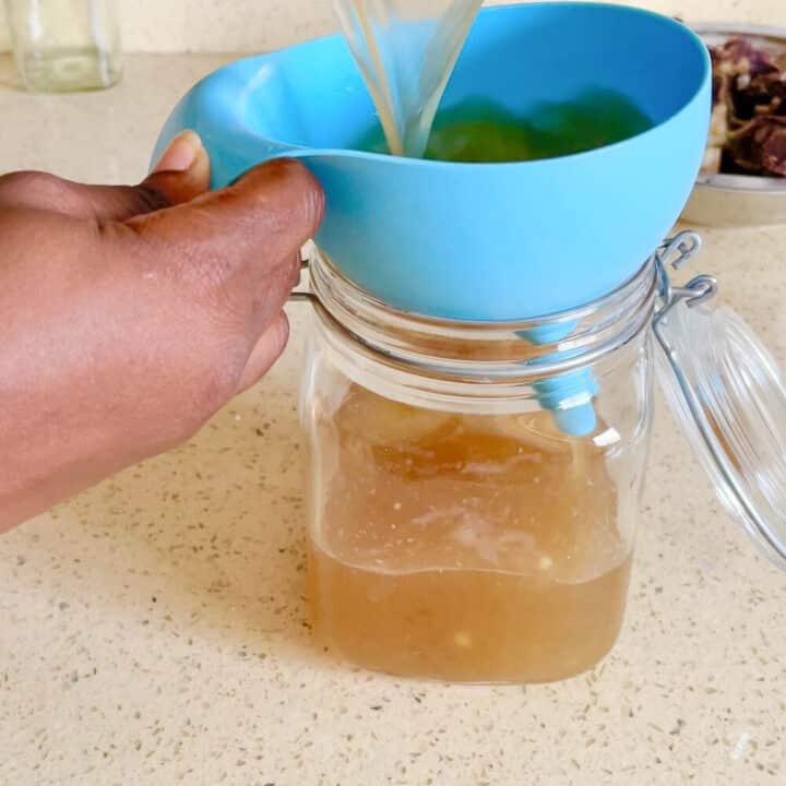 Pouring the beef stock into jar with a blue funnel.