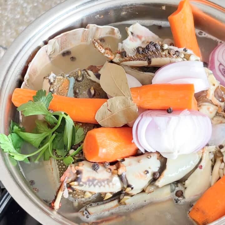 Lobster stock in a pot with carrots, bay leaves, peppercorns, onions and parsley.