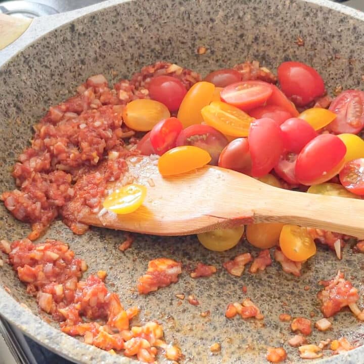 Fried onions, garlic, cherry tomatoes and tomato paste in a pan.
