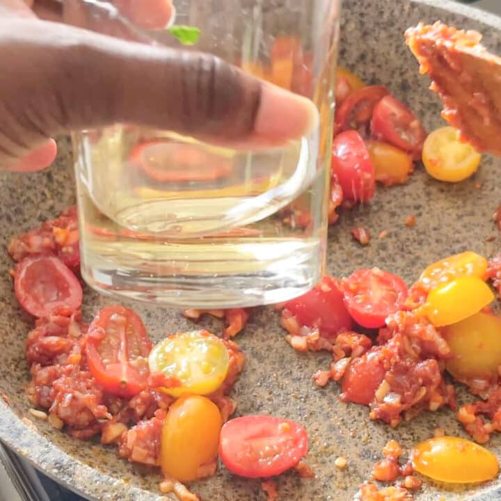 Wine in a glass over a pan with cherry tomatoes.