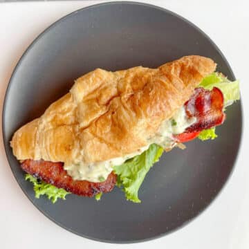 BLT croissant sandwich with garlic mayo sauce on a round black plate.