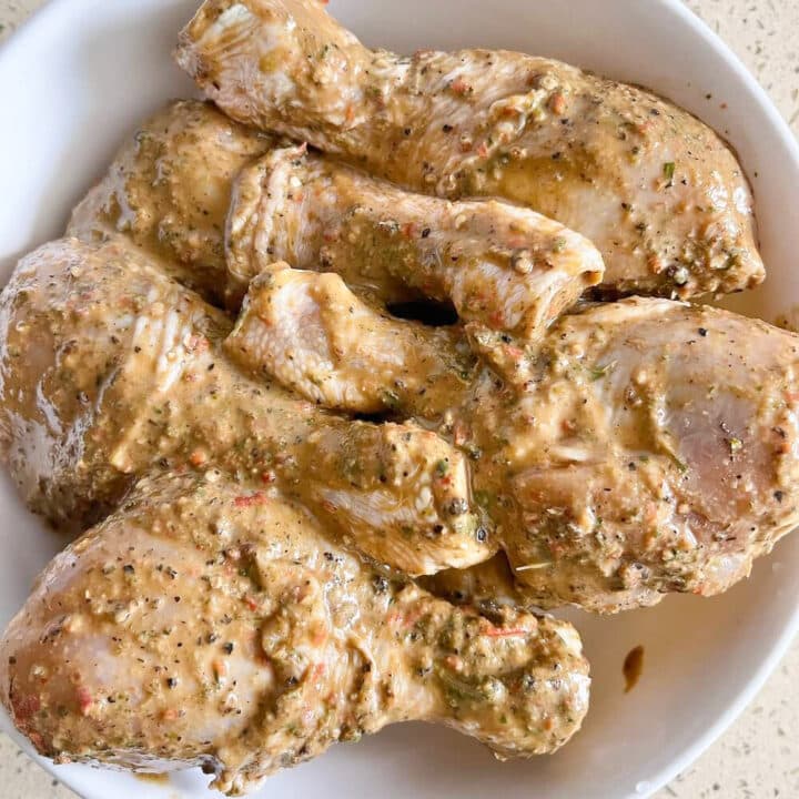 Chicken drumsticks marinated in a white round plastic bowl.