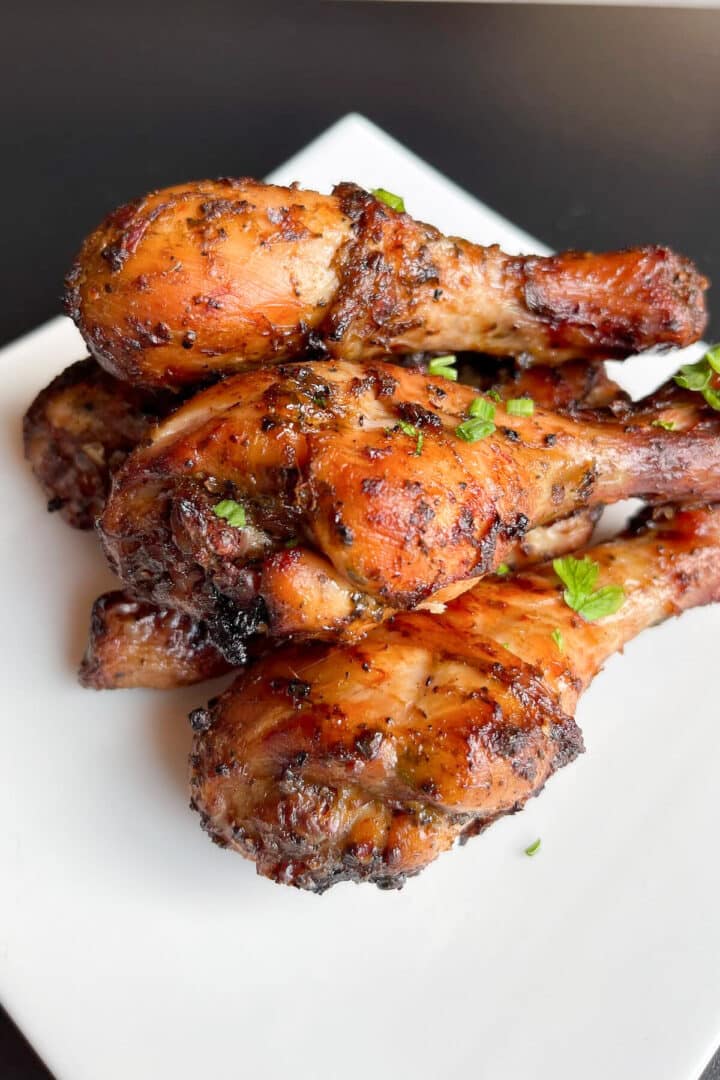 Grilled chicken drumsticks on a white plate with chopped parsley sprinkled on top.