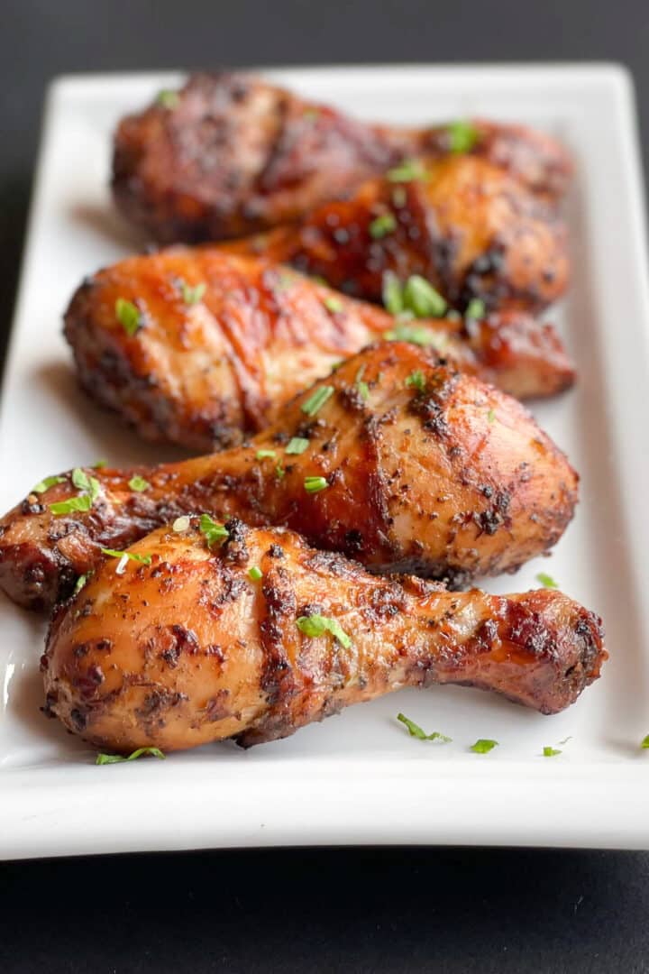 Grilled chicken drumsticks on a white rectangular plate with chopped parsley sprinkled on top.