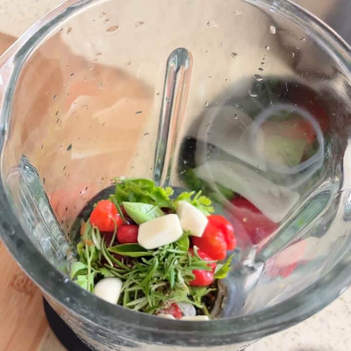 Garlic, herbs and peppers for marinade in a glass blender.