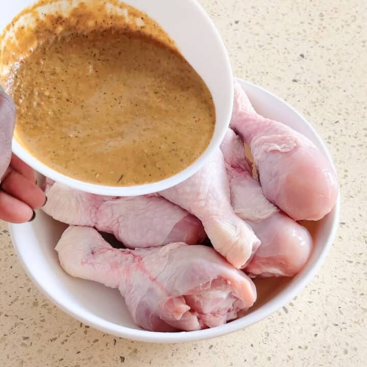 Marinade in a small round ceramic bowl and raw chicken drumsticks in a large white plastic bowl.