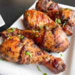 Grilled chicken drumsticks on a white rectangular plate with chopped parsley sprinkled on top.