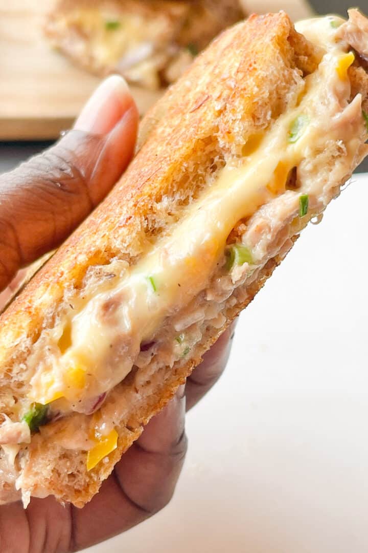 A cross section of a tuna melt showing melted cheese, bits of bell pepper and spring onions.