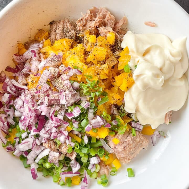 Chopped bell peppers, onions, spring onions, mayo and tuna in a white bowl.