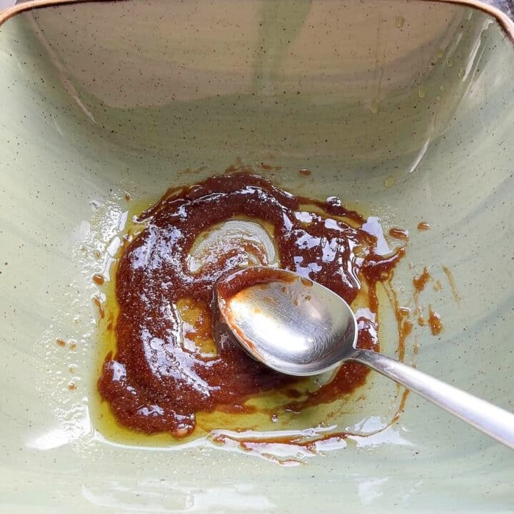 Balsamico, olive oil and parmesan cheese mixed in a green bowl with a spoon ion the side.